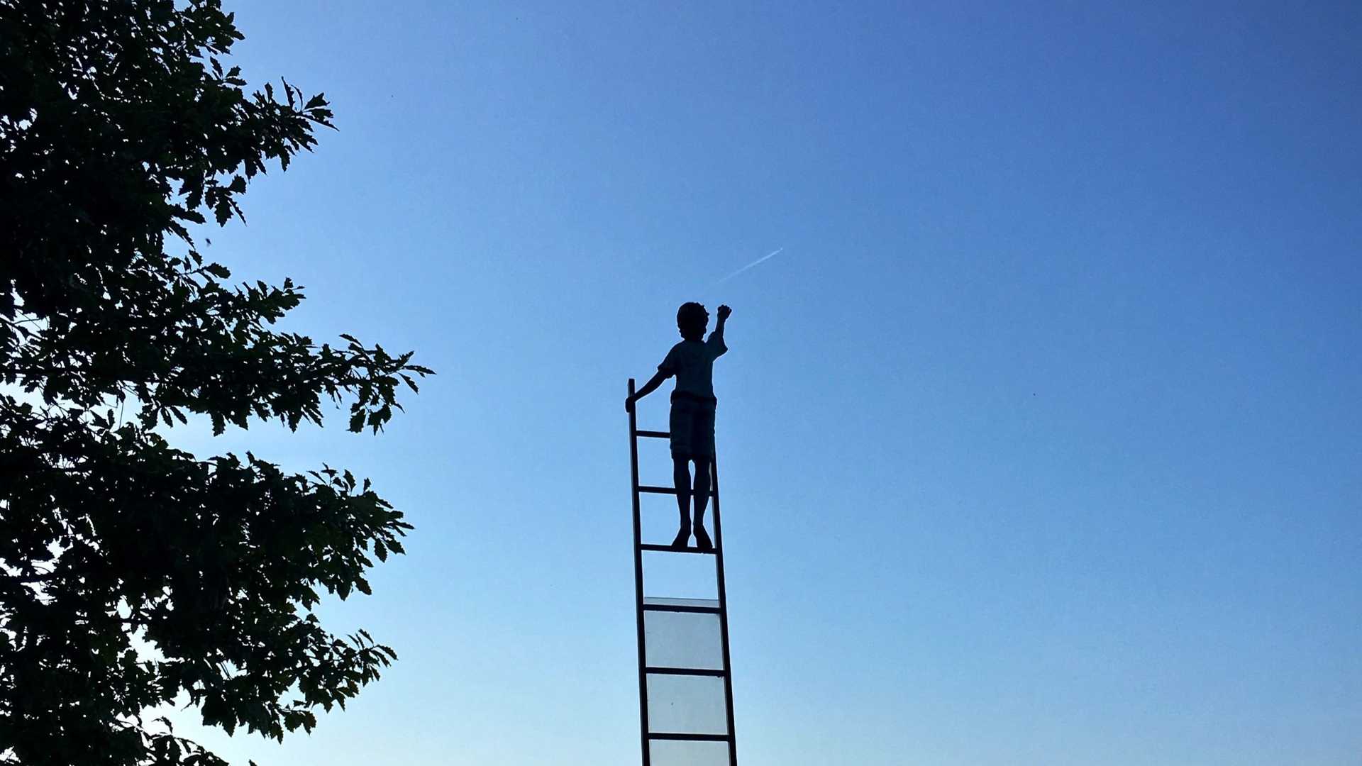 A young person is standing on a latter that directs to the blue sky