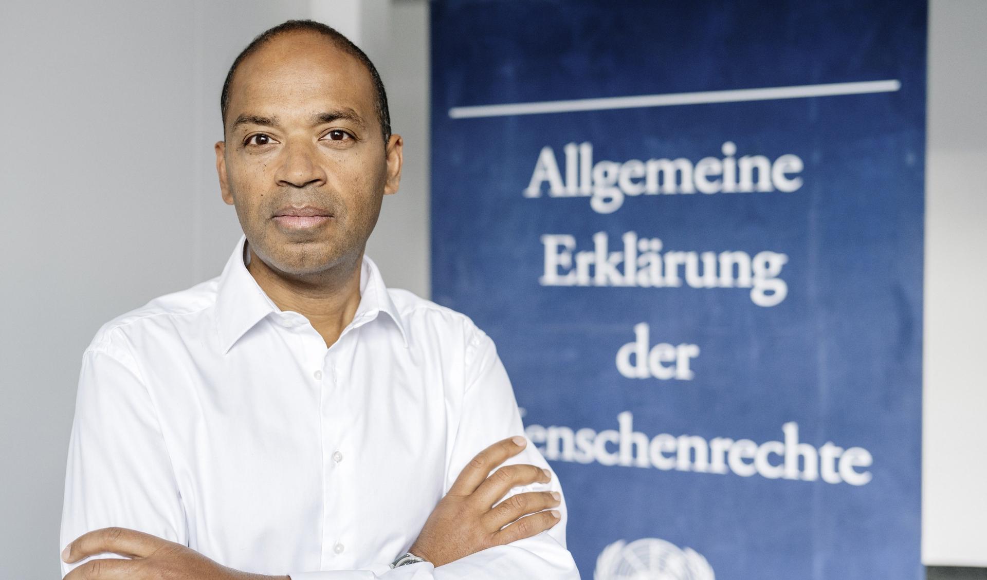 Markus Beeko is standing in front of the Declaration of Human Rights as a poster and looks into the camera