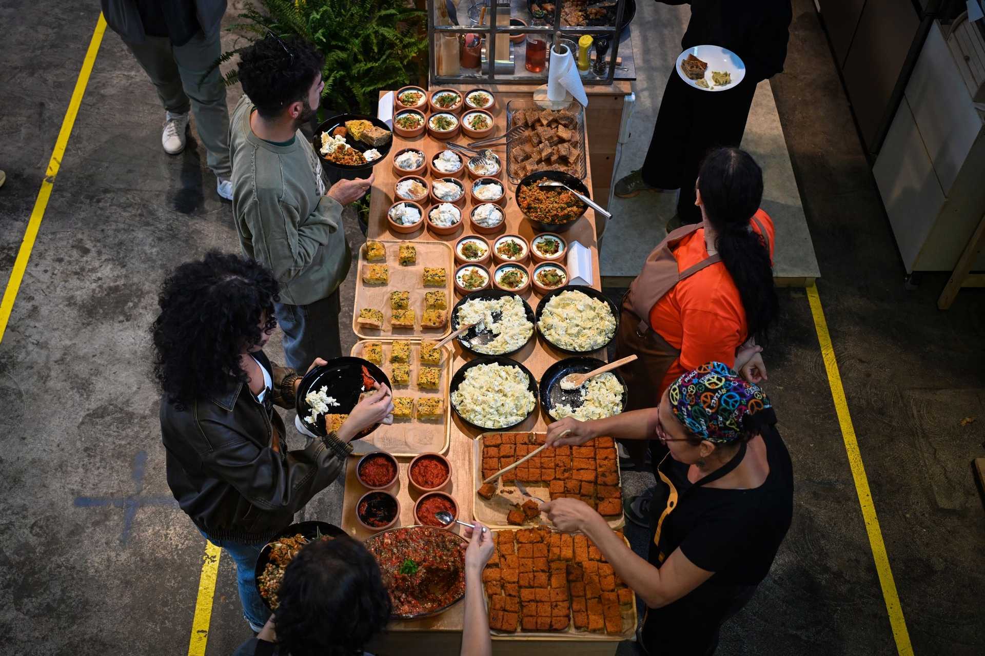 Many people are standing at a table. Some are getting food, others are serving food.