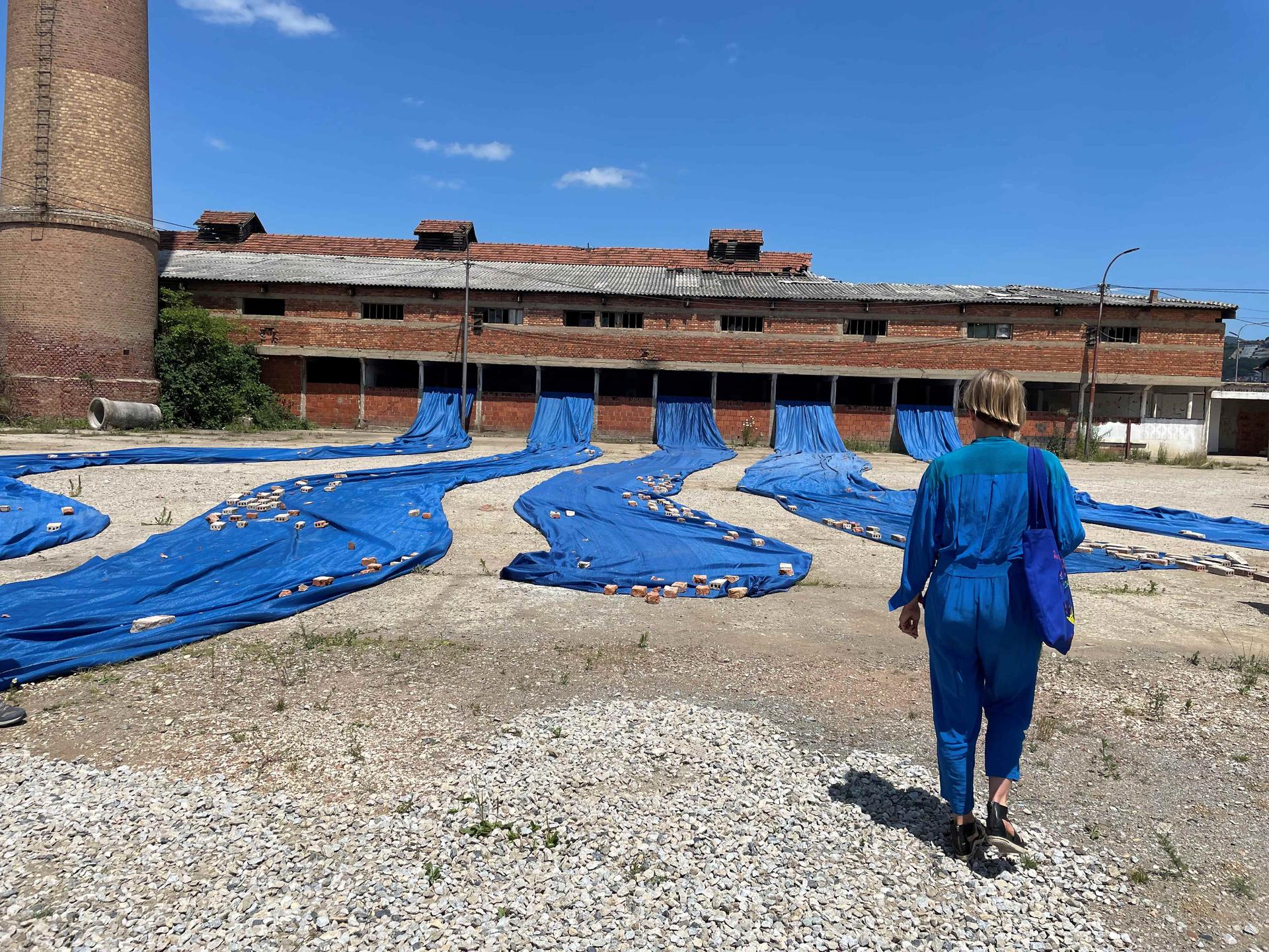 Big strips of blue fabric flowing like water out of a brick factory