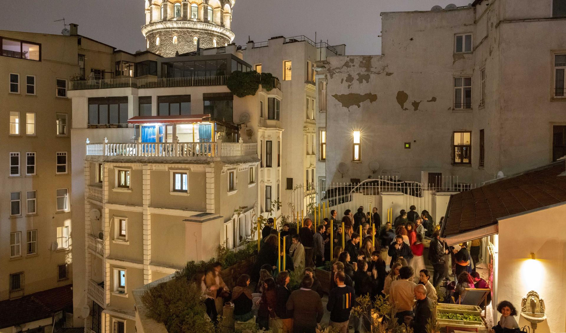 A terrace in the nightime in Istanbul is bustling. In the back you see Istanbuls houses