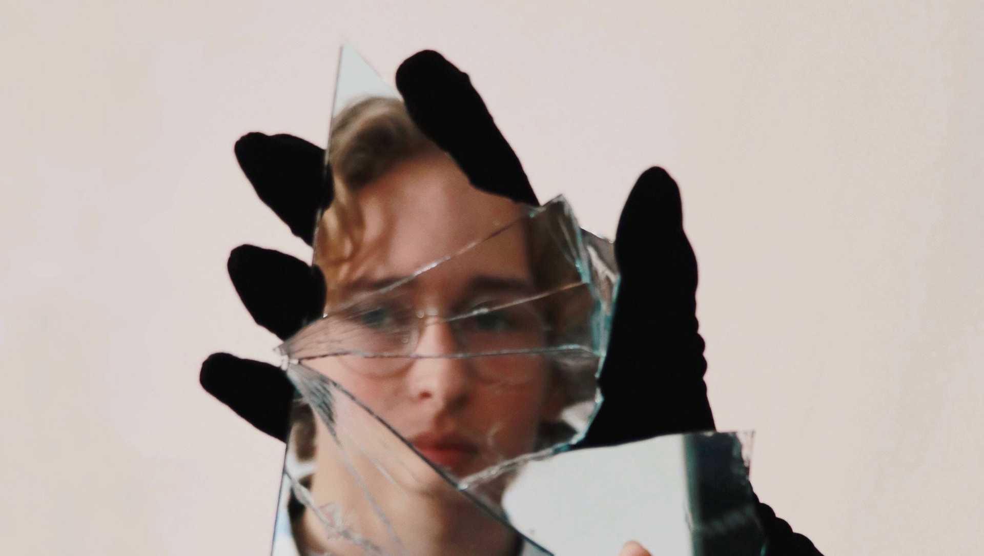 A person is looking into a piece of a mirror that another hand with black gloves is holding