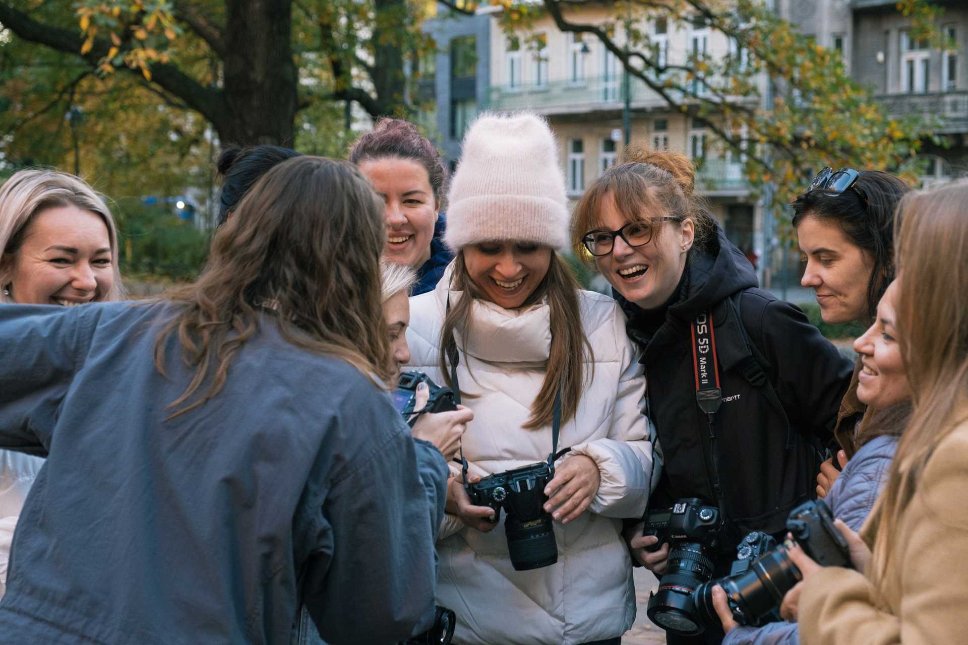 A group of women and girls gathered and are looking at a camera to see pictures one of them made. They are laughing.