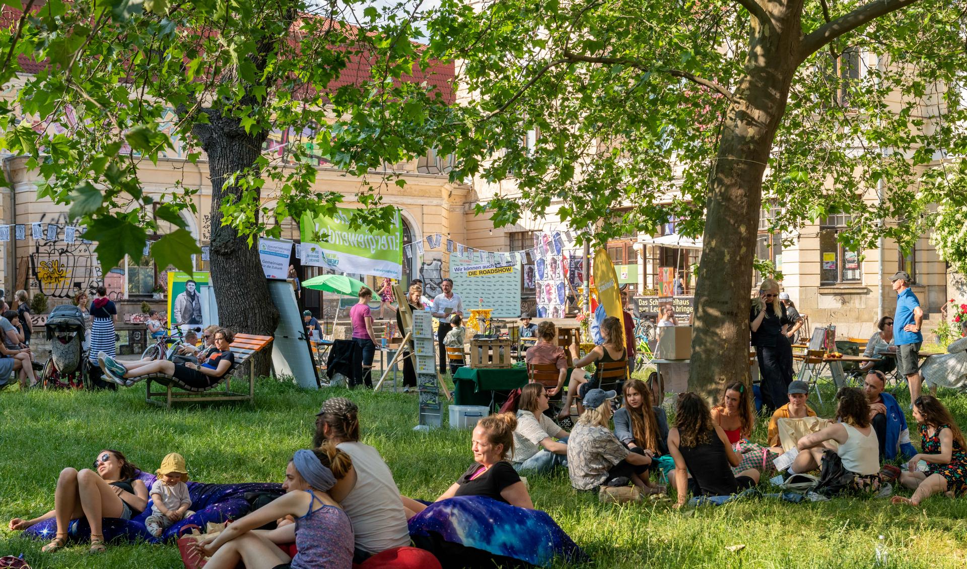 A green garden in a courtyard of a theater. It is sunny weather, people are sitting outside and talking to each other,