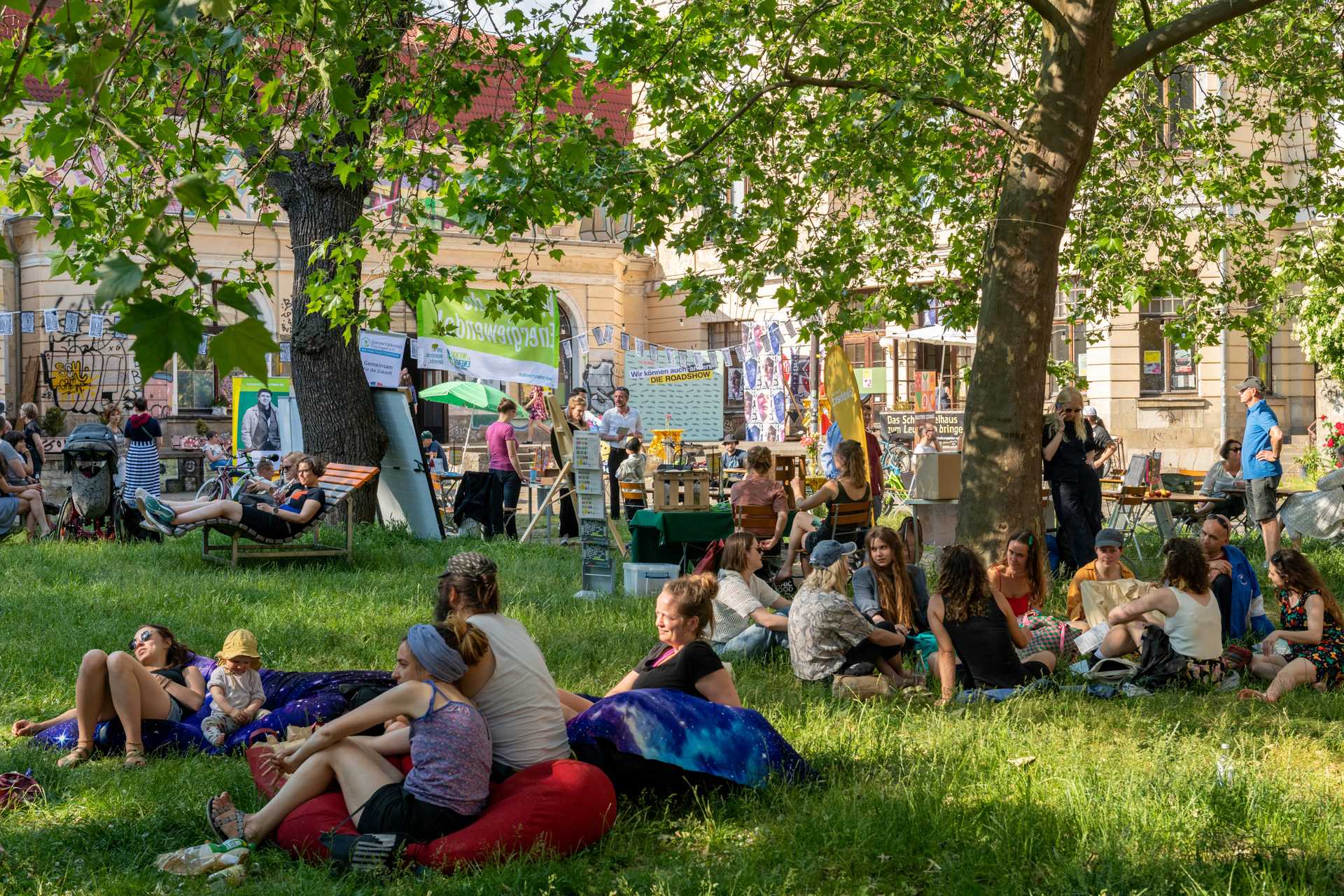 A green garden in a courtyard of a theater. It is sunny weather, people are sitting outside and talking to each other,