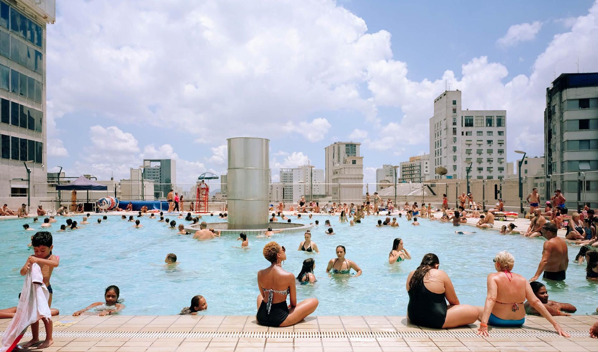 A swimming pool on a roof in Sao Paulo is showing people swimming and resting at the pool on the top of the city