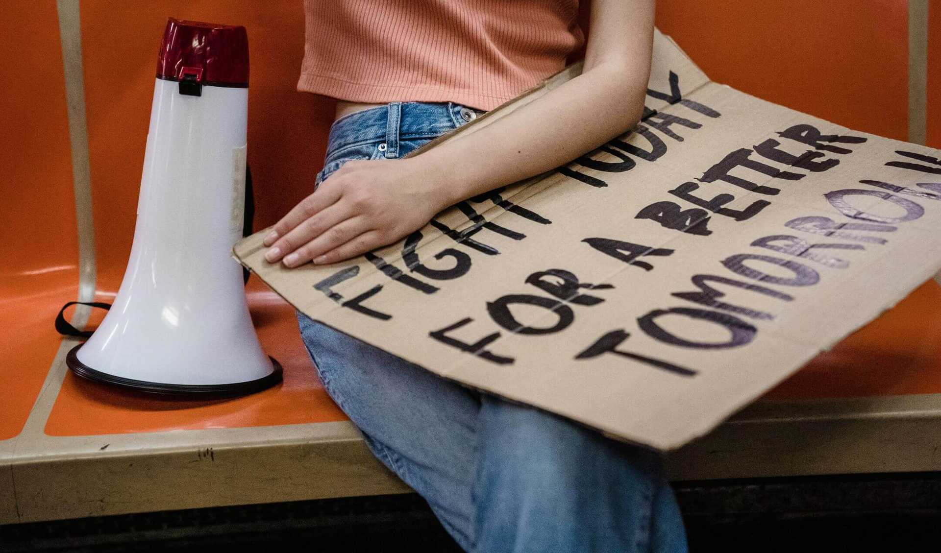 A person is sitting on a bench with a poster on her laps and a megaphone