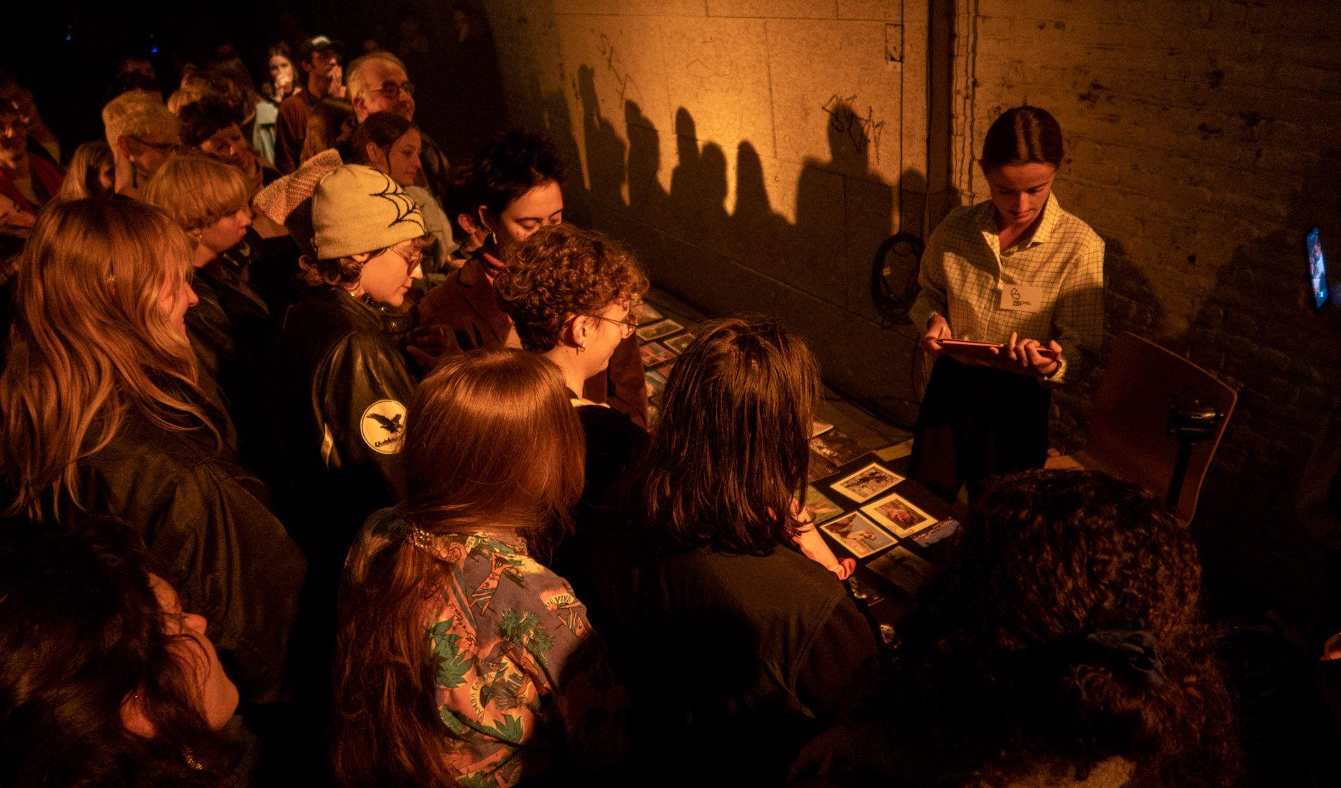 People are standing in fron of a long table and are looking on pictures on the table and other pieces of art