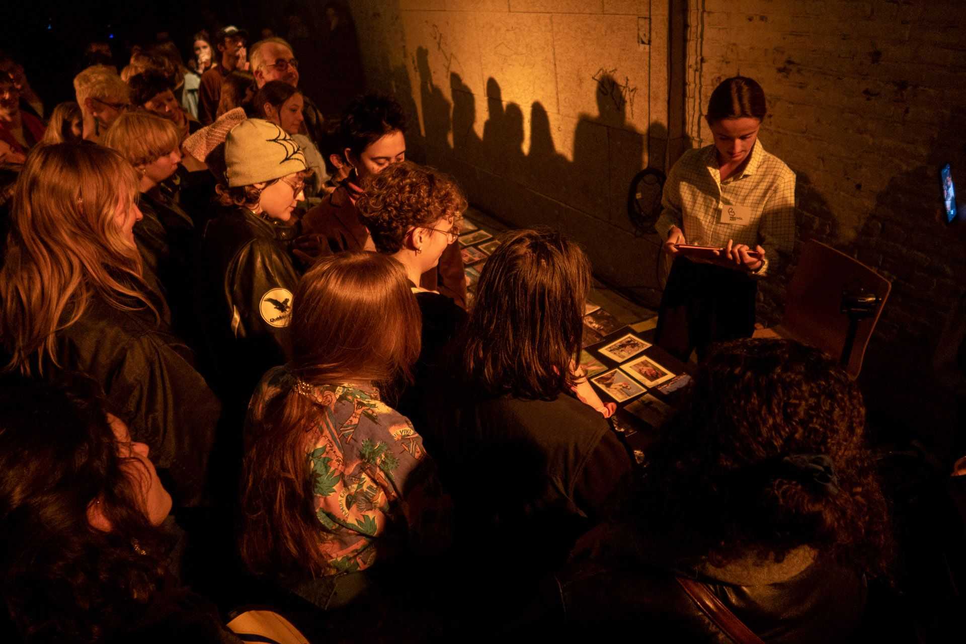 People are standing in fron of a long table and are looking on pictures on the table and other pieces of art