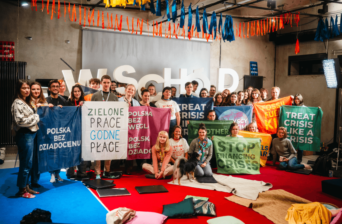 A group of people holding up signs in front of a sign saying "Wschód"