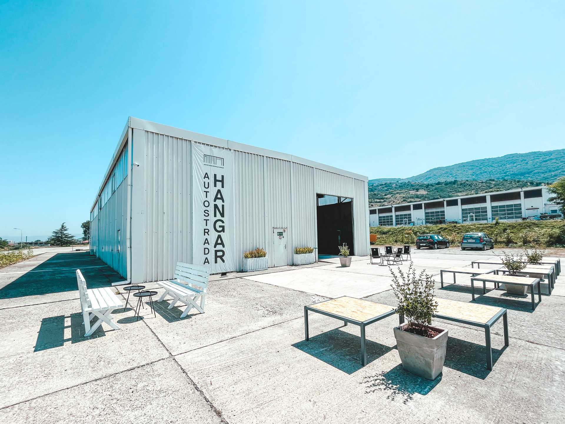 The hangar of Autostrada biennale. In fron you see an open air meeting spot with tables and benchesr 