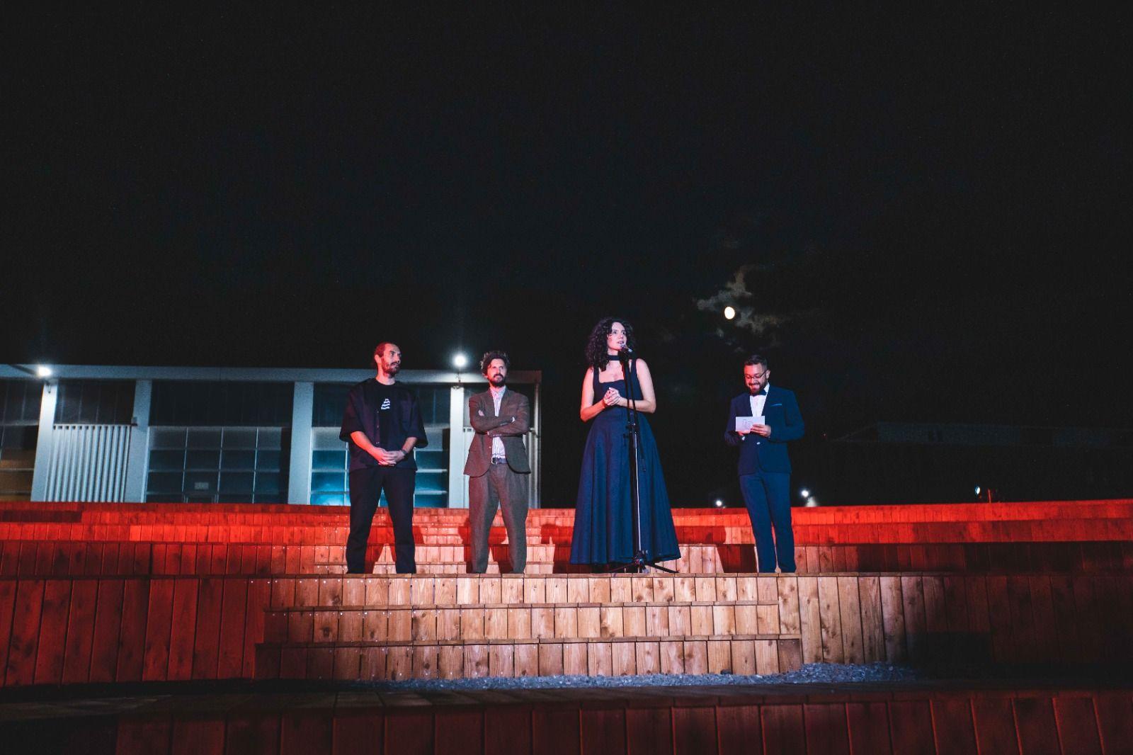 Four persons are standing, they are beautifully dressed and one of them is holding a speech