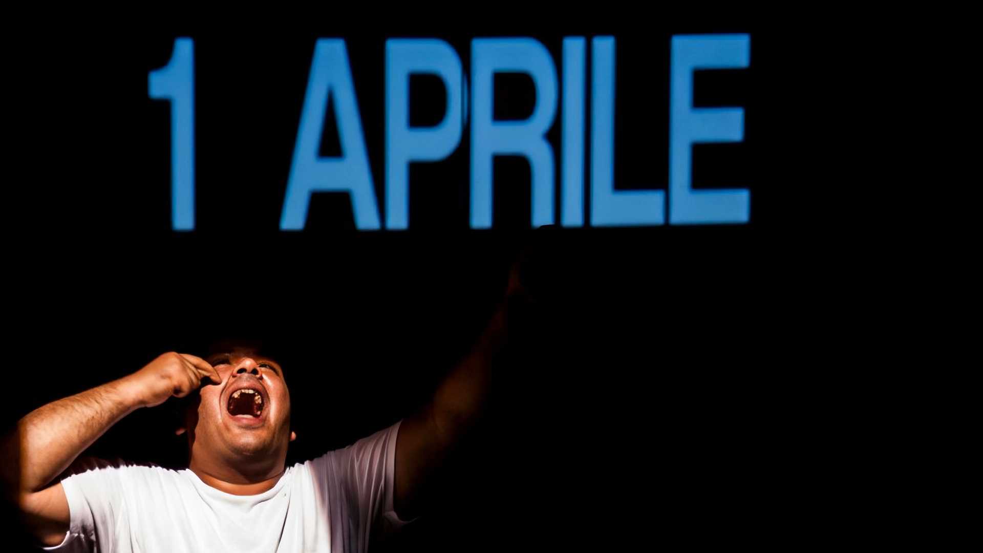 A person is yelling in the left corner of the picture, above him it's written in big blue letters "1 April". He seems to be on a stage