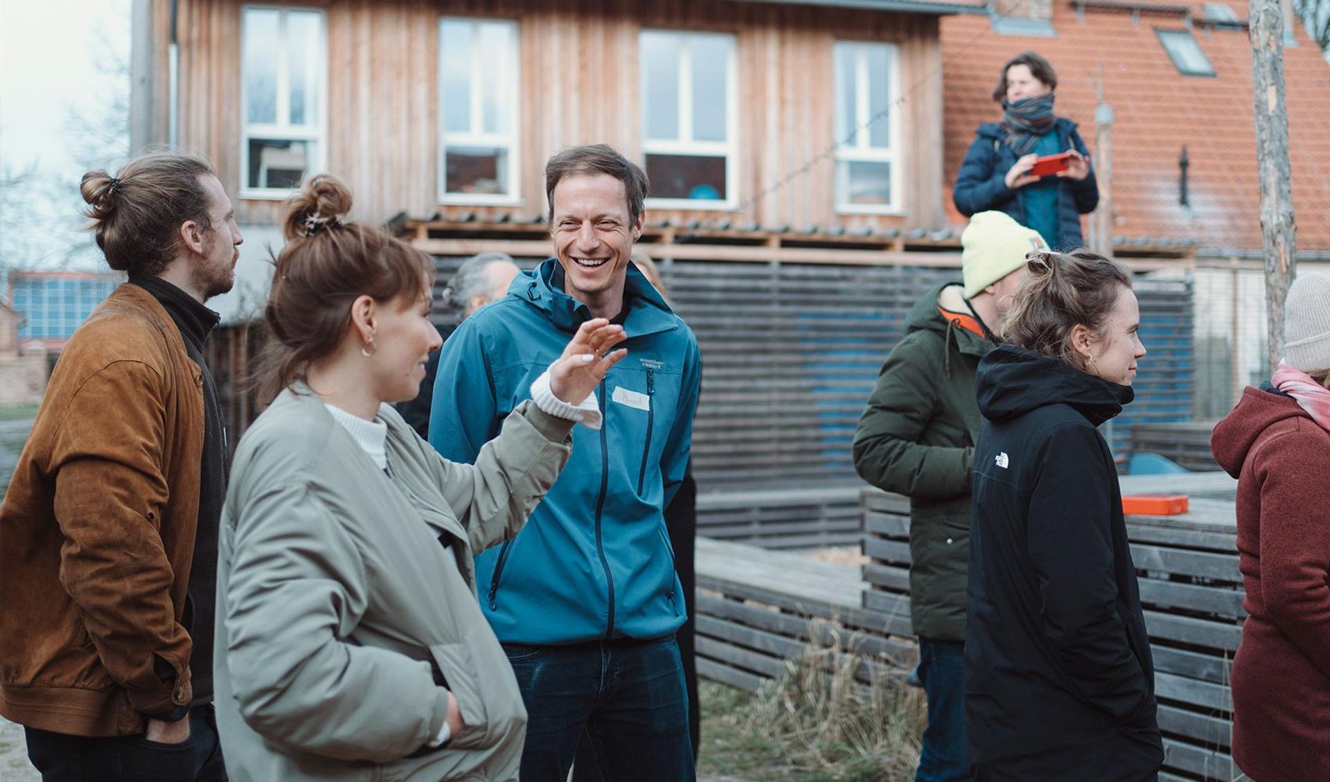 People are standing outside on a construction side in a smaller town oder village. They are talking to each other and are laughing.