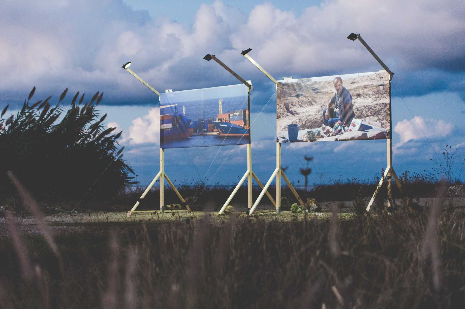 Two big billboaards are displaying pictures of a harbour and a person sitting in a rocky landscape