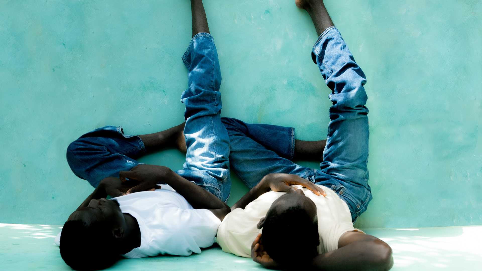Two persons are sitting on the ground and leaning on a wall