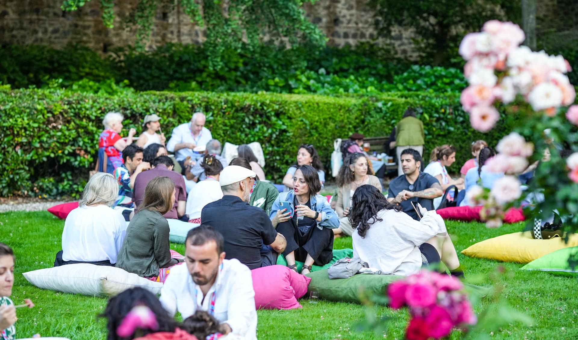 People are sitting on green grass on the grounds of the Academy - it is summer