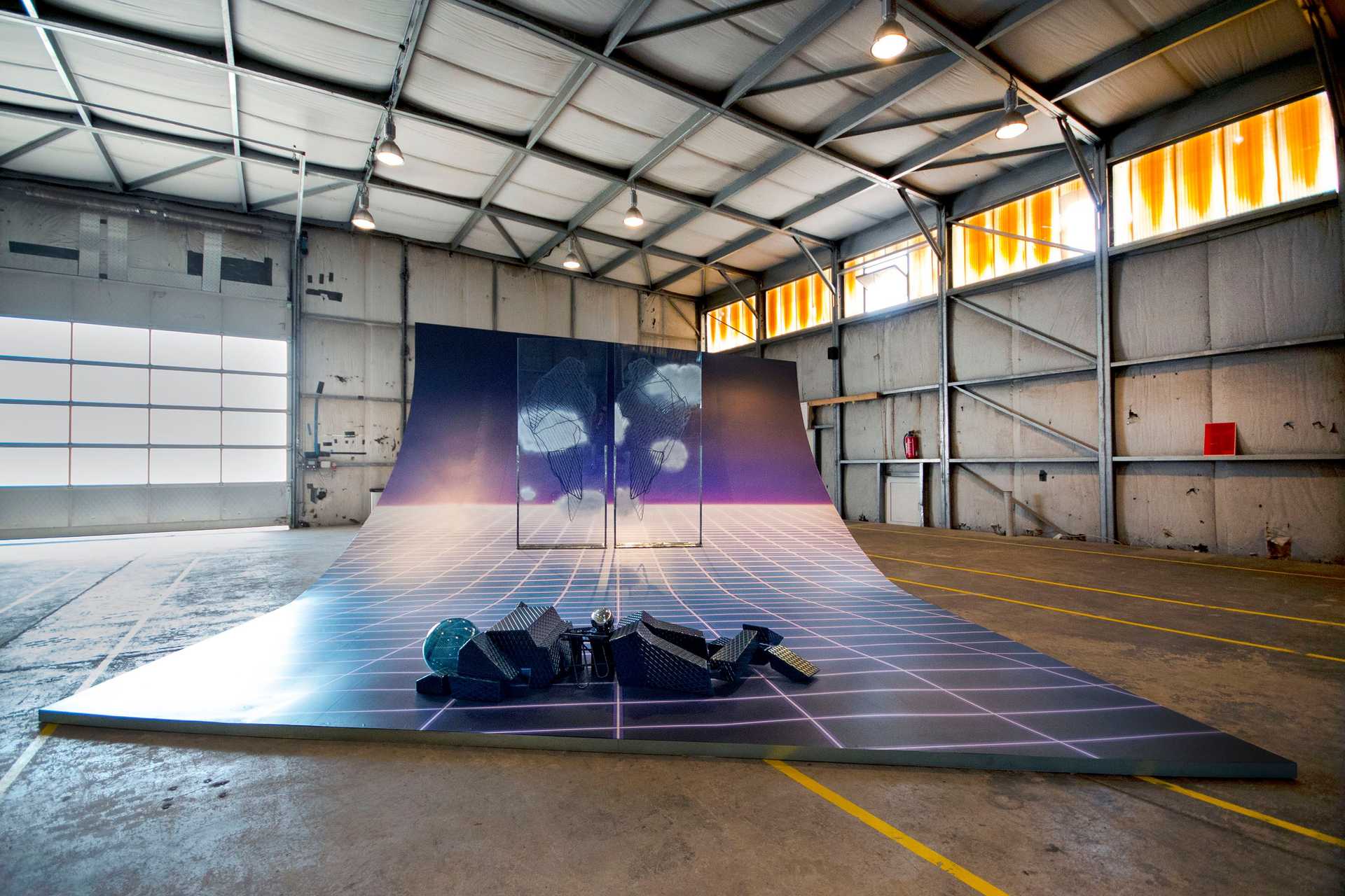 A huge art installation is displayed in an empty hangar.