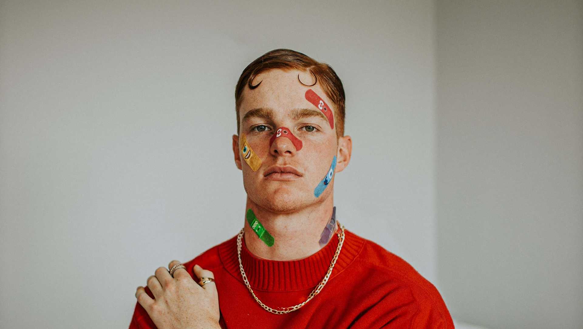 A man on a bed with three arms and many plasters on his face
