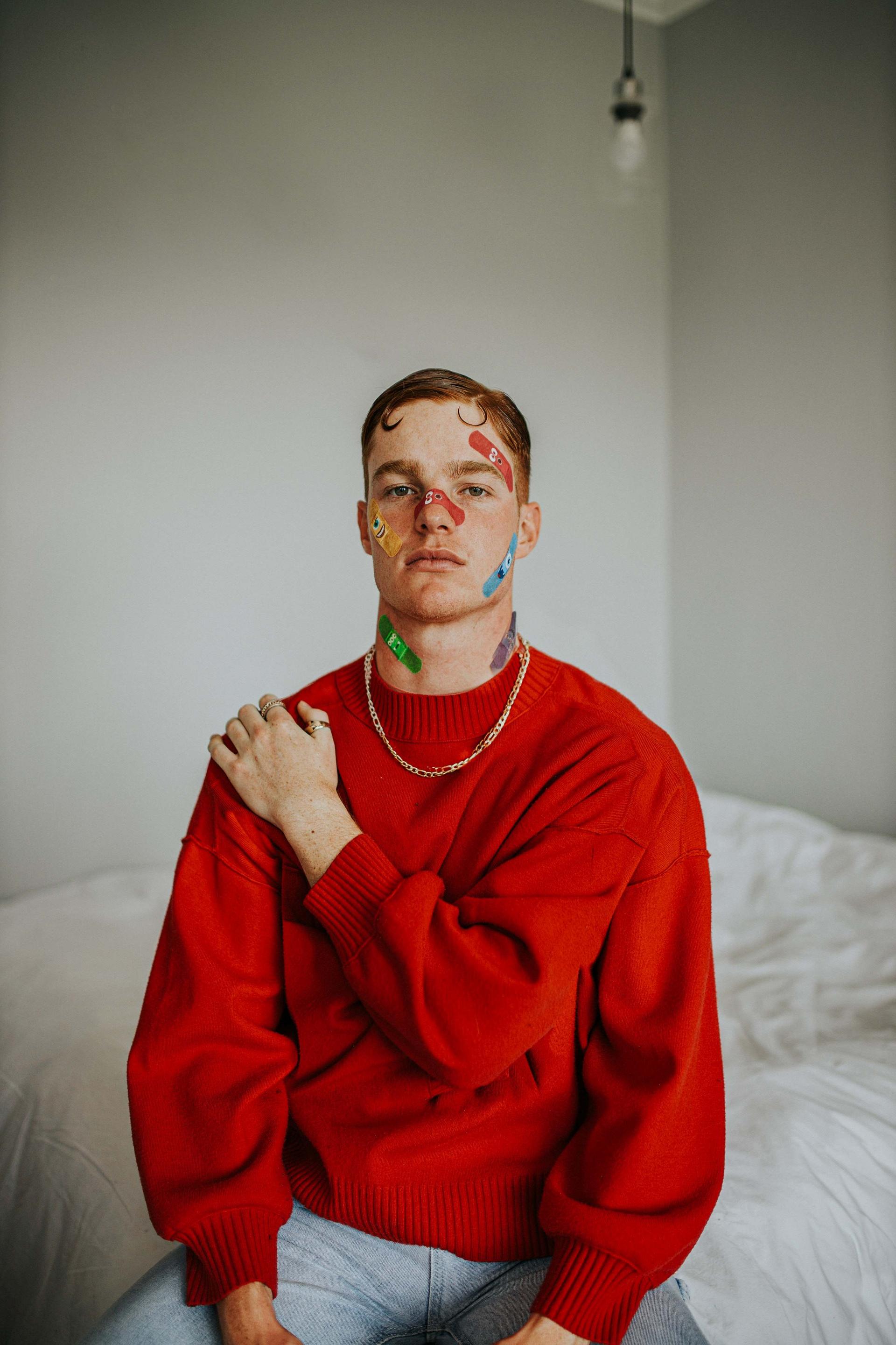 A man on a bed with three arms and many plasters on his face