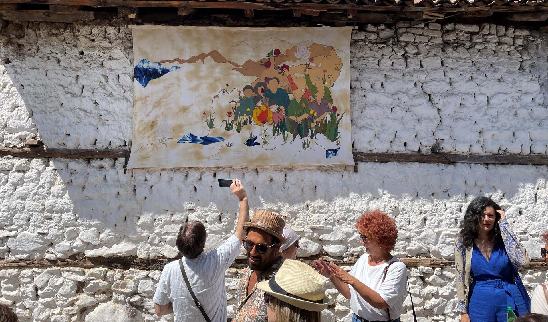 People are standing outside in the front of a wall and are looking onto a paicture at the wall.