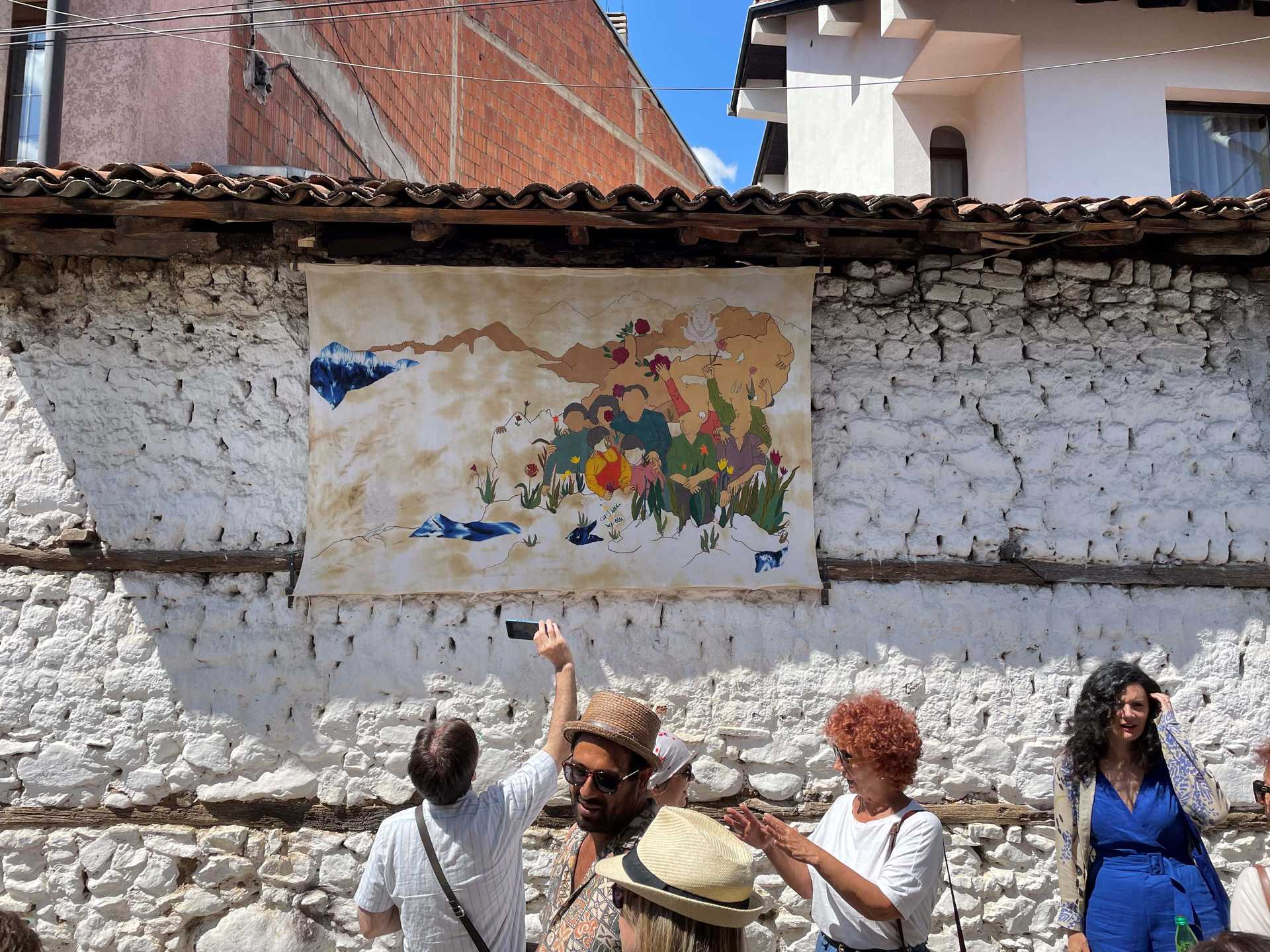 People are standing outside in the front of a wall and are looking onto a paicture at the wall.