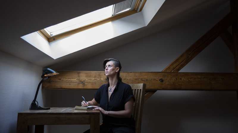 Camila Nobrega is sitting in a room and looks up to the sky through a window in the roof.