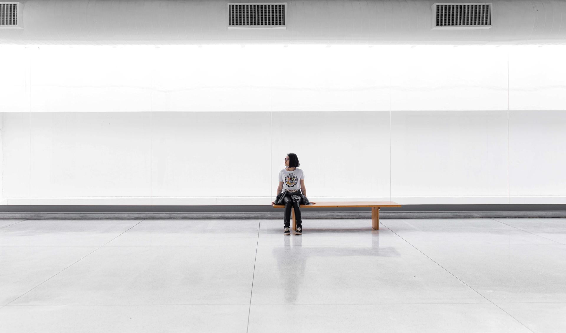 A person is sitting in a big white hall. She seems to wait for something.