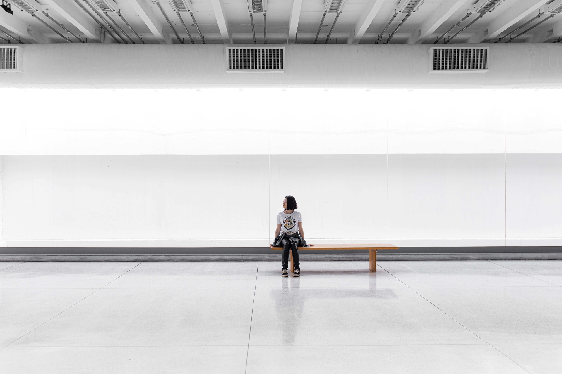 A person is sitting in a big white hall. She seems to wait for something.