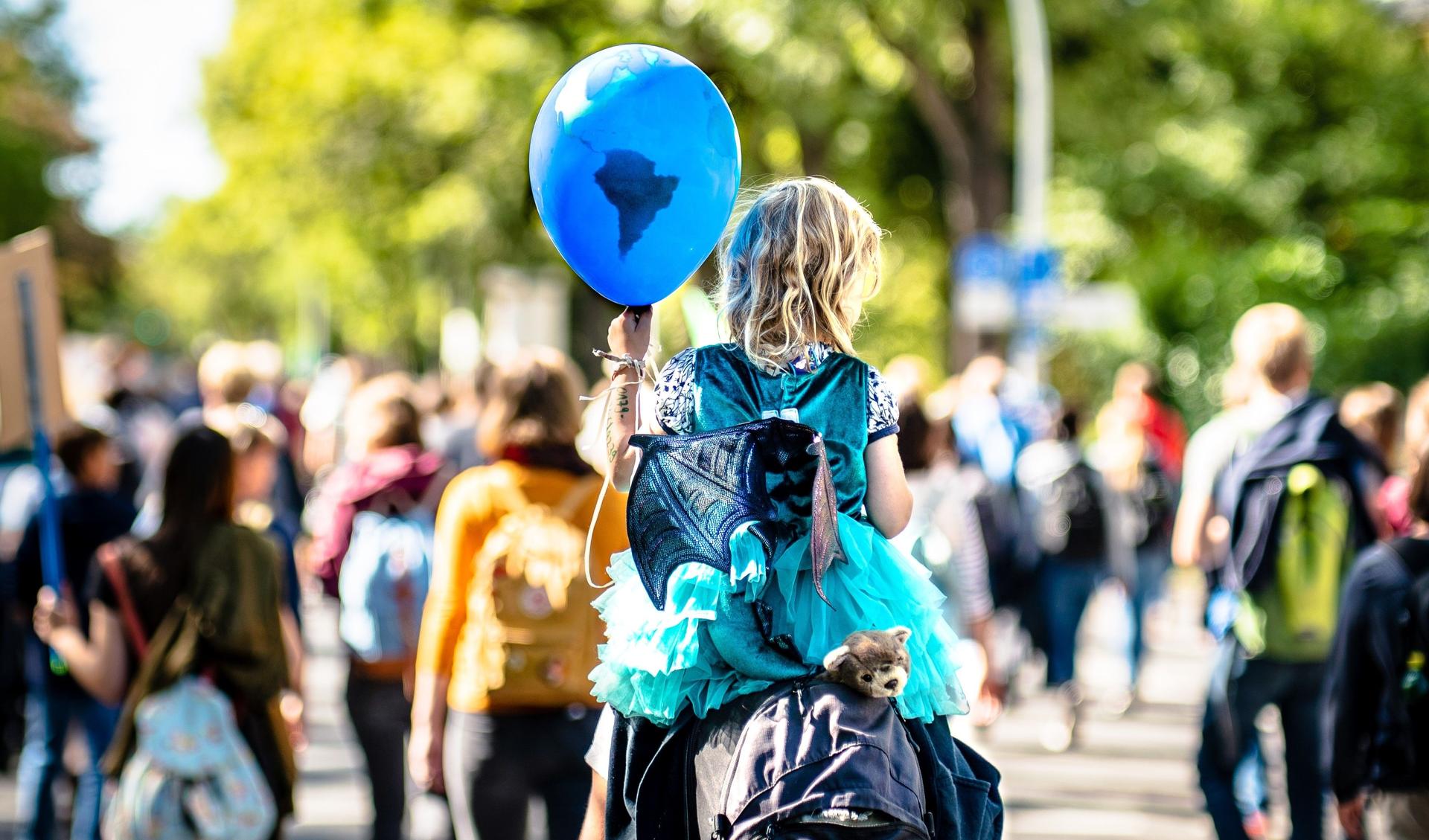 A demonstration - a child is sitting on the shoulders of a grown-uo person. It holds a ballon in its hands that looks like the earth but in blue.