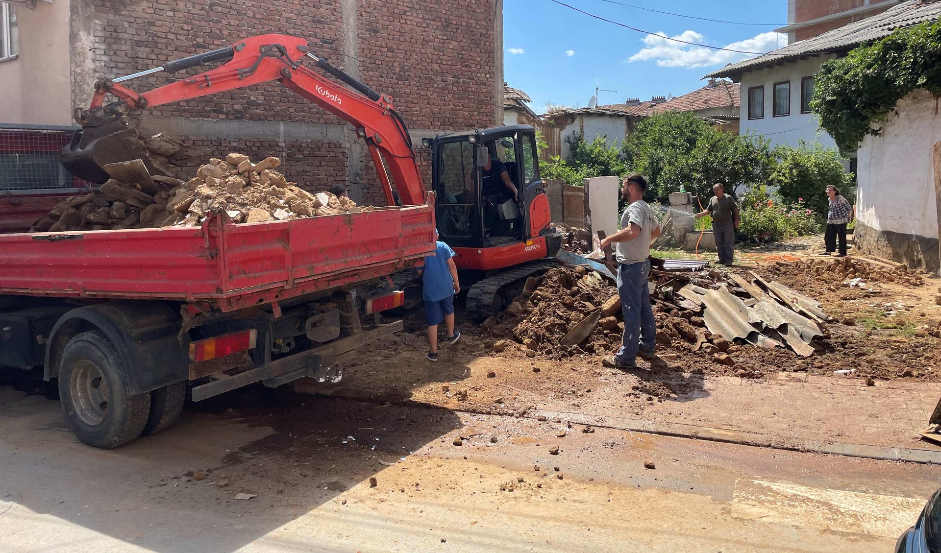 A mount of rubble lies at a sport where there was a house. Workers are pickung up the rubble.