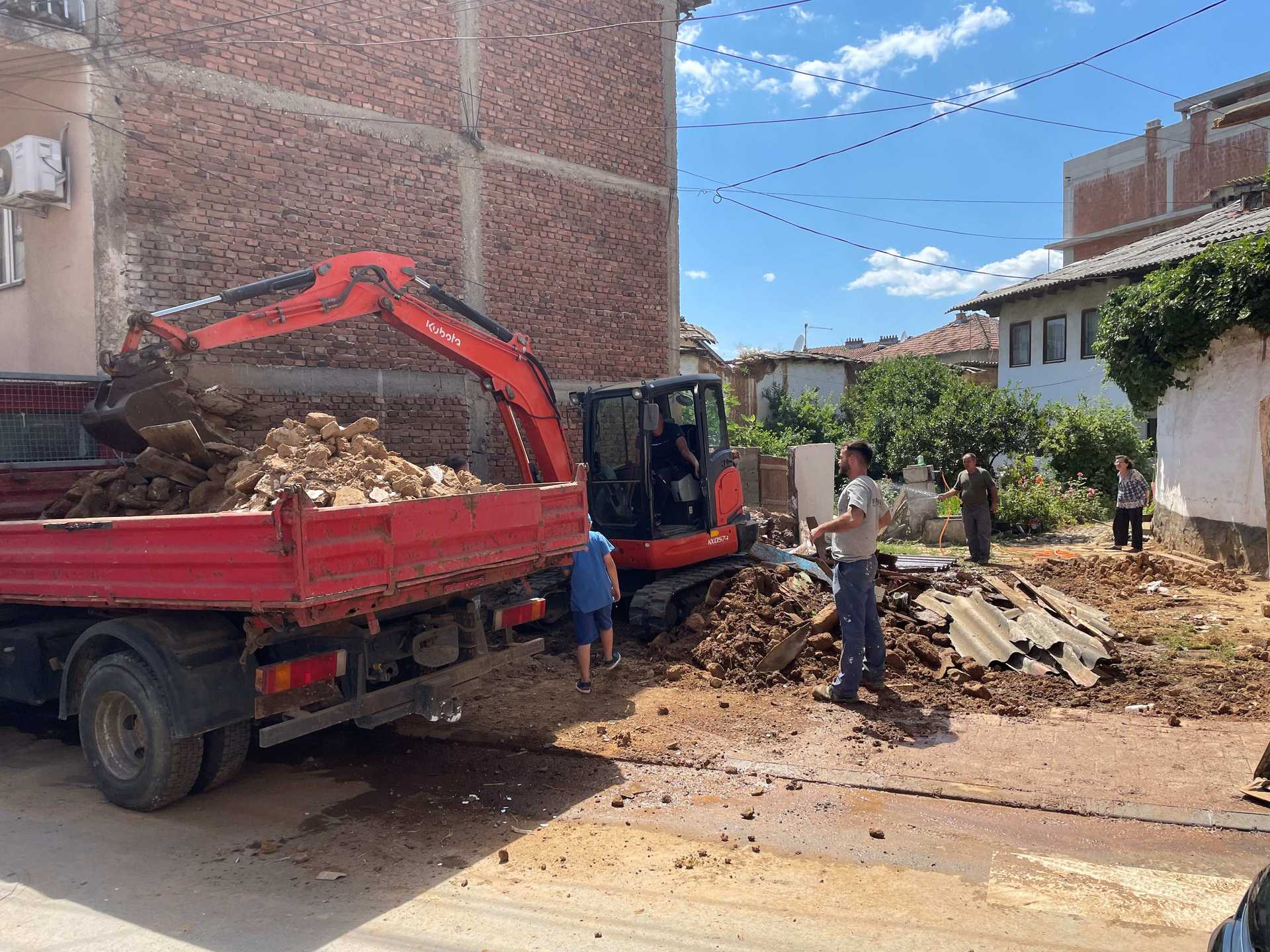 A mount of rubble lies at a sport where there was a house. Workers are pickung up the rubble.