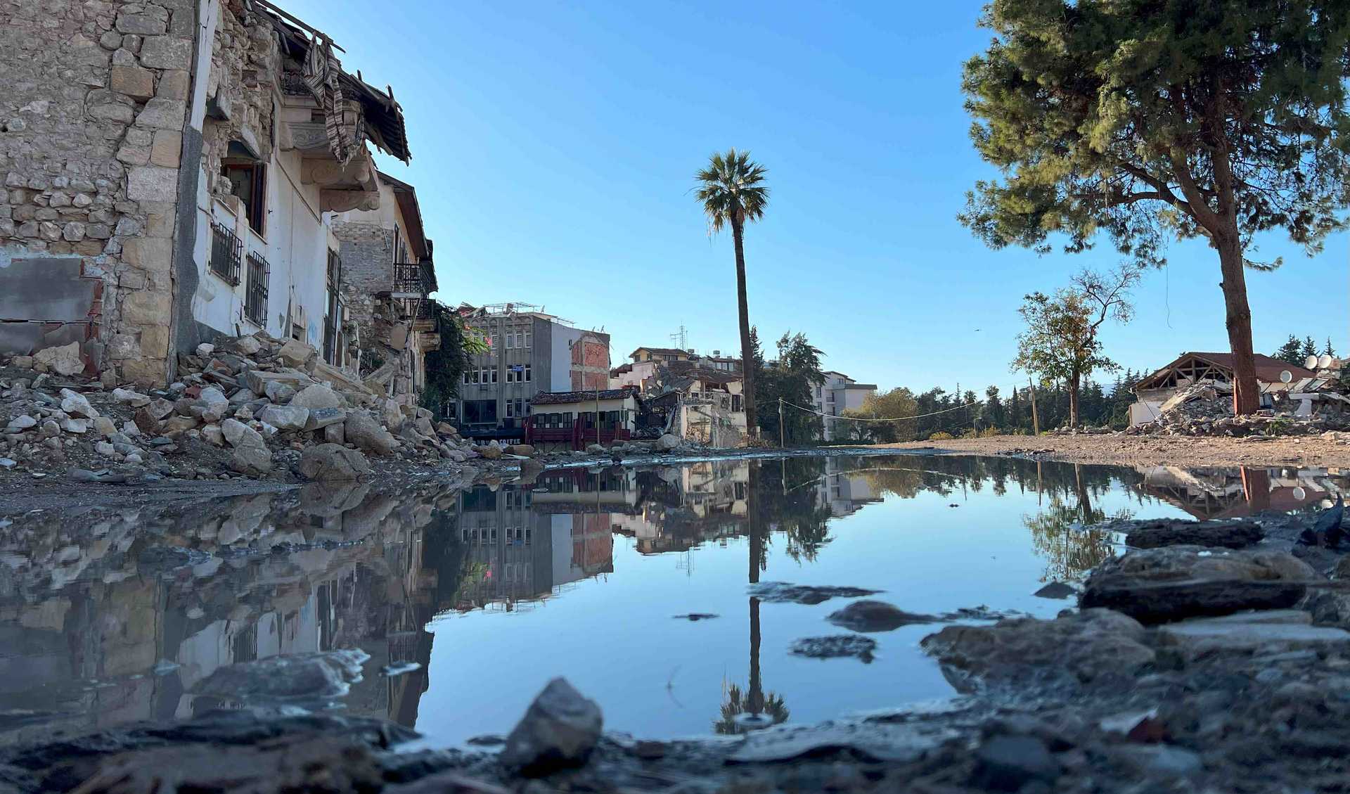 A puddle reflects a landscape of ruins and a palm tree