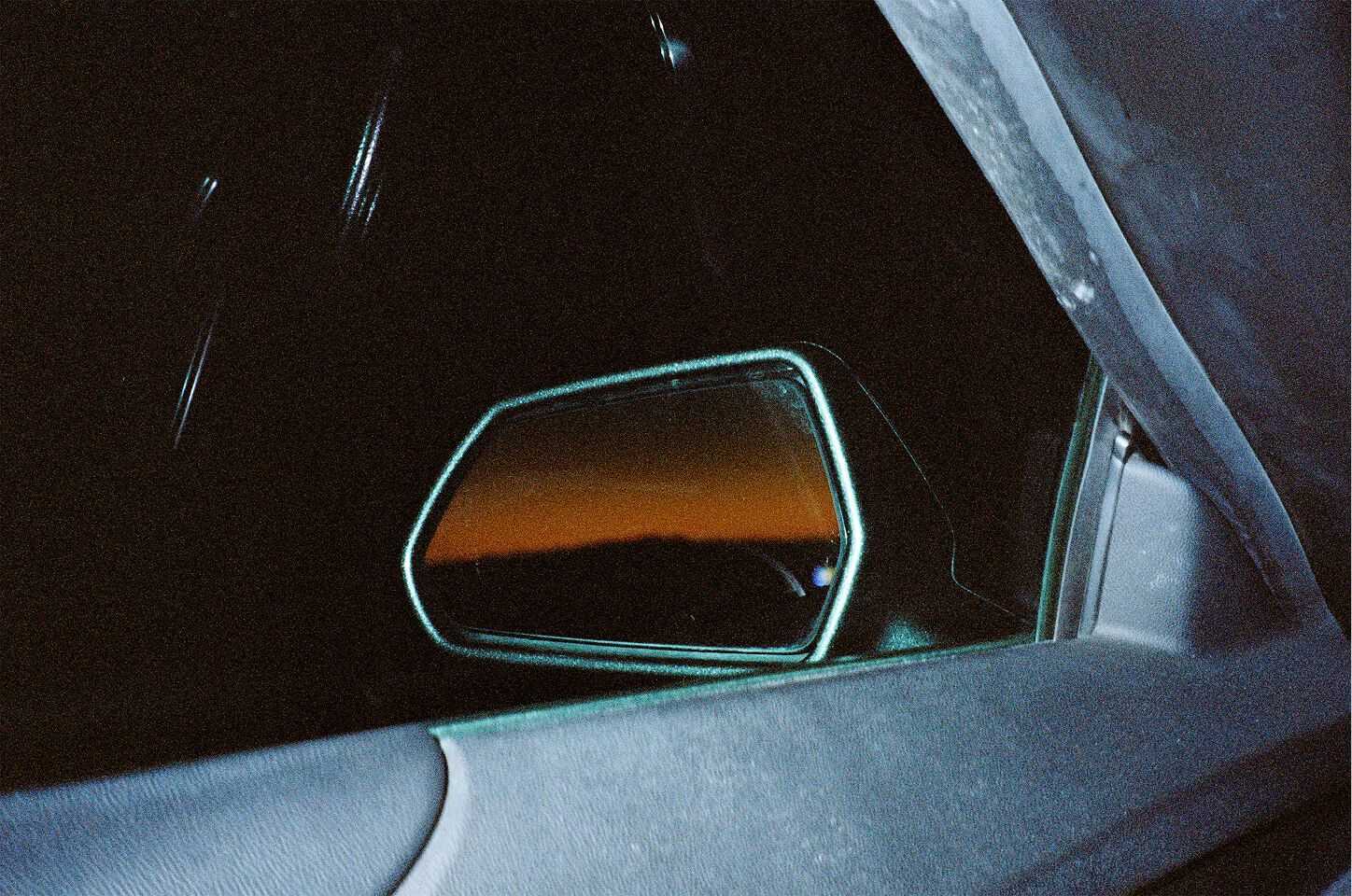 A rear mirror pictured from inside is showing a sunset
