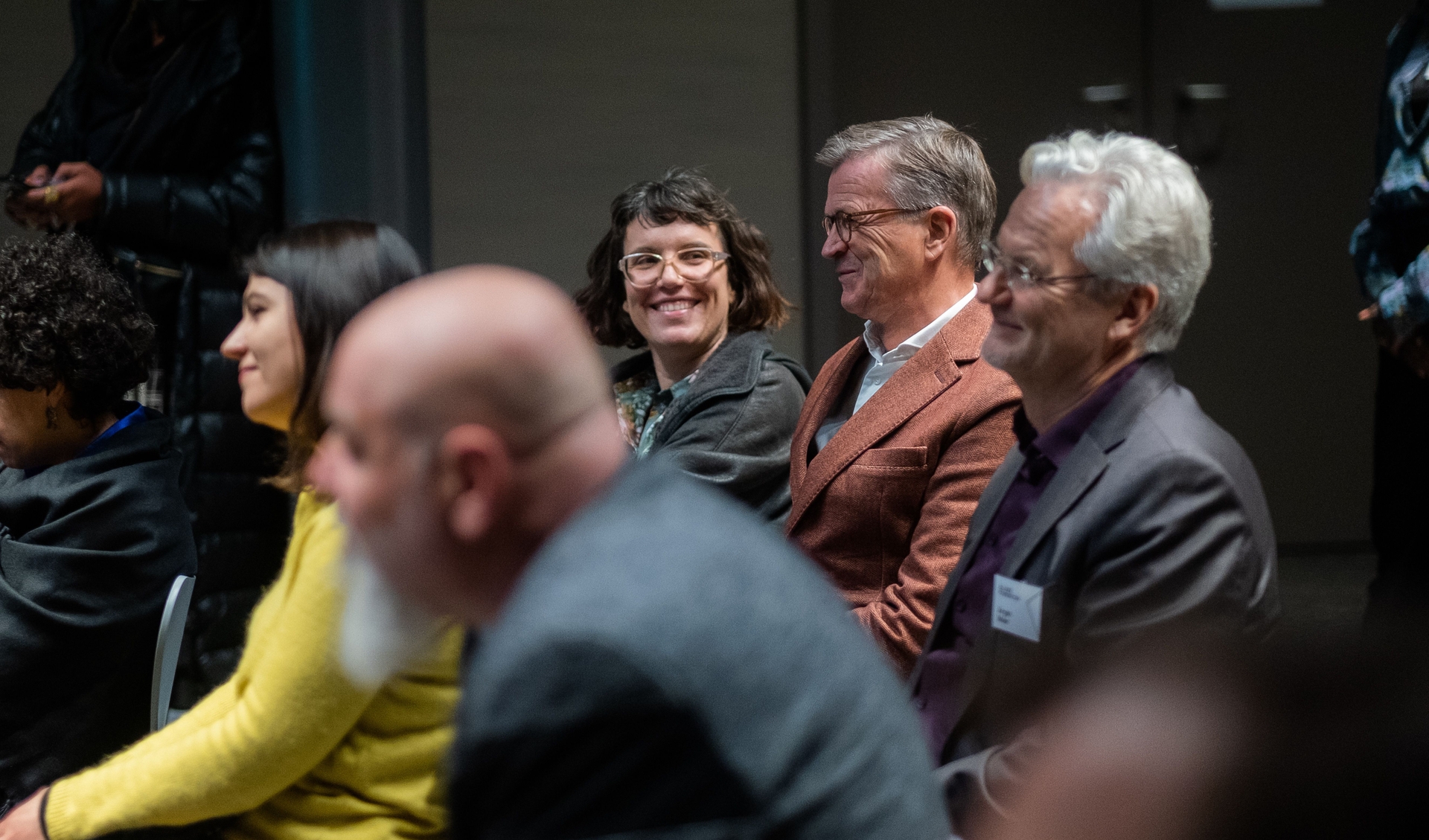 Mitglieder des Managements und des Kuratoriums sitzen in einer Reihe im Saal 